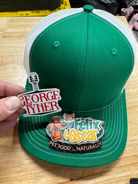 Full-color name and logo patches displayed with a green-and-white trucker hat as an example