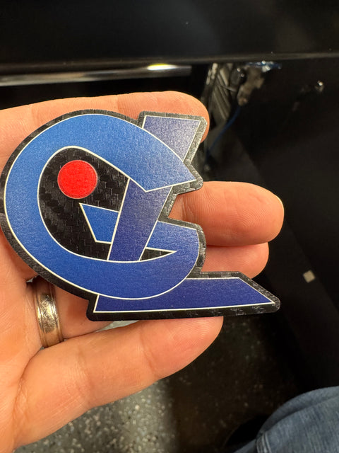 Blue geometric logo patch with a red dot held in a hand