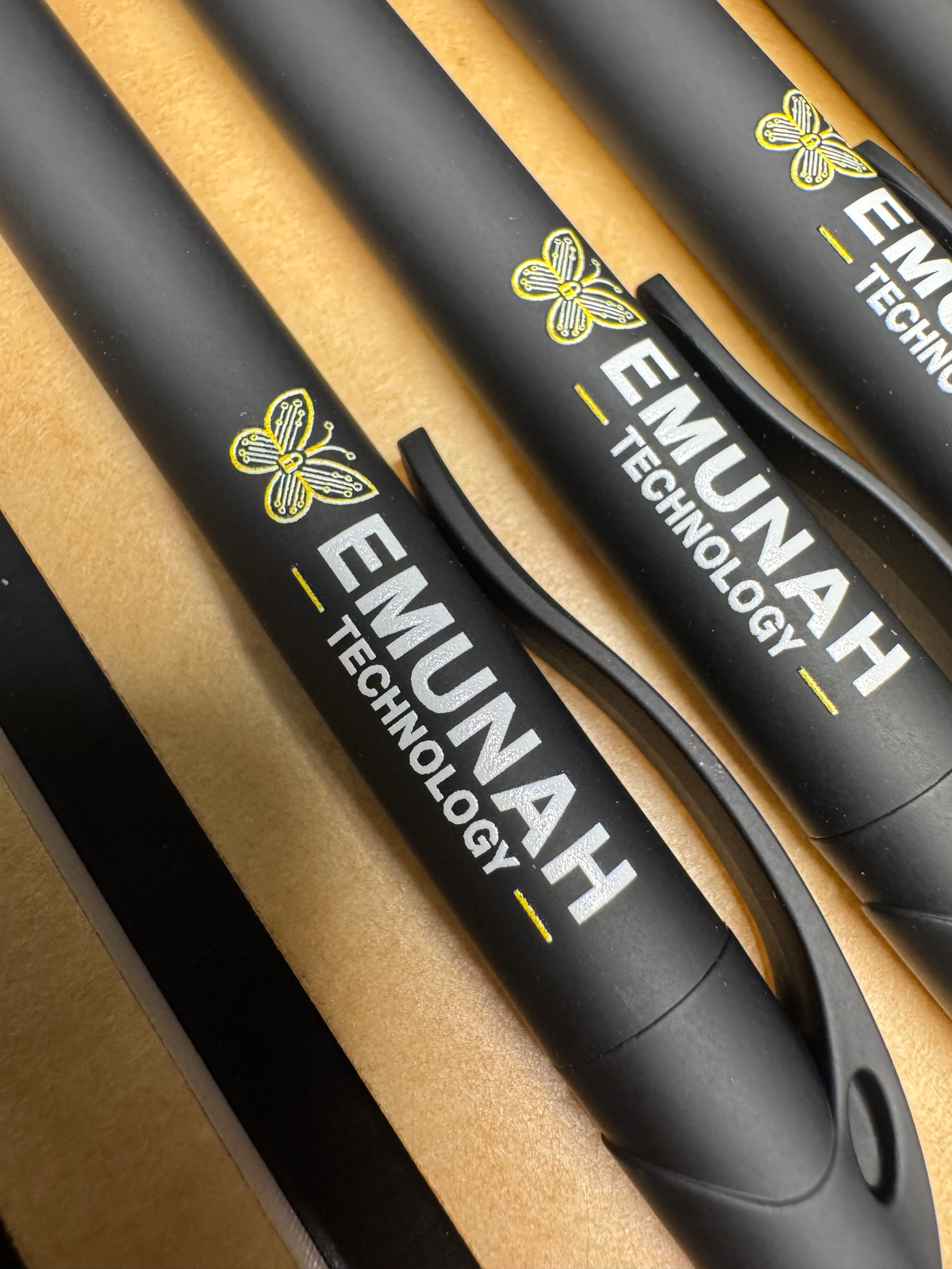 Close-up of black pens with Emunah Technology printed branding.